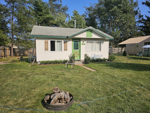 view of front of property featuring a front yard, fence, an outbuilding, and a fire pit