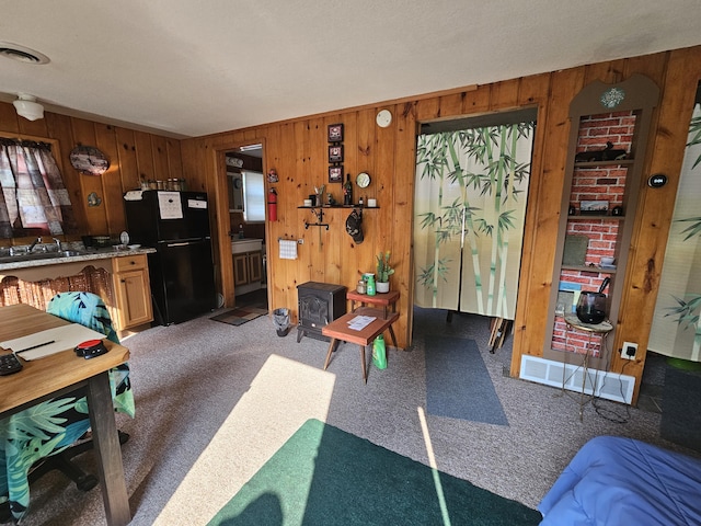 interior space featuring a wood stove, visible vents, freestanding refrigerator, and carpet floors