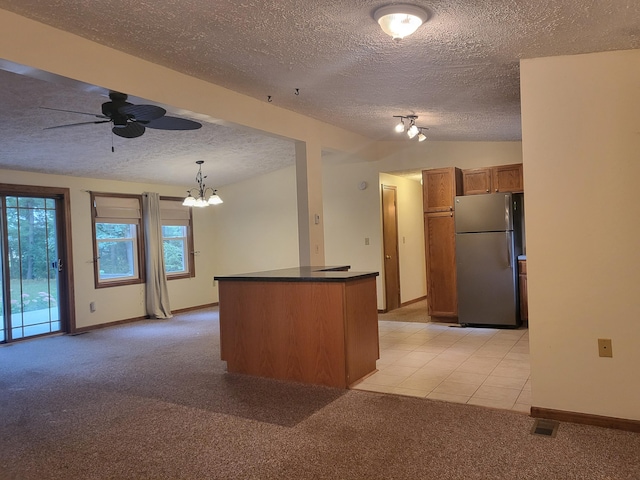 kitchen with light carpet, brown cabinets, dark countertops, freestanding refrigerator, and ceiling fan