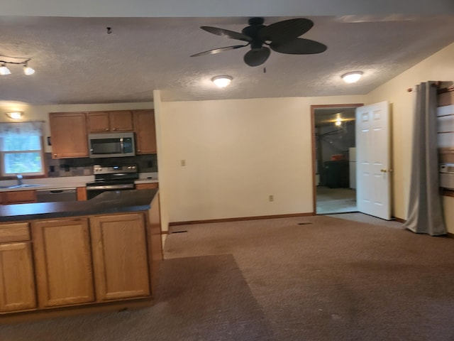 kitchen with dark countertops, carpet, stainless steel appliances, brown cabinetry, and a textured ceiling