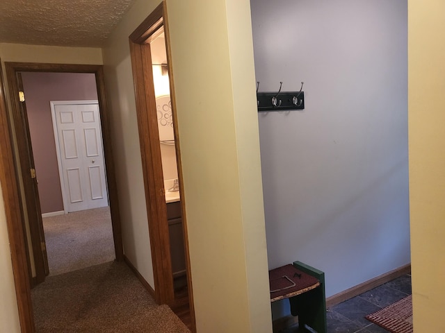 hall featuring carpet flooring, baseboards, and a textured ceiling