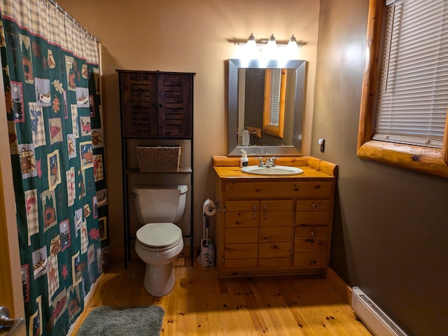 bathroom with a baseboard heating unit, hardwood / wood-style flooring, toilet, and baseboards