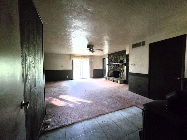 living area with visible vents, a wainscoted wall, carpet flooring, a fireplace, and a ceiling fan