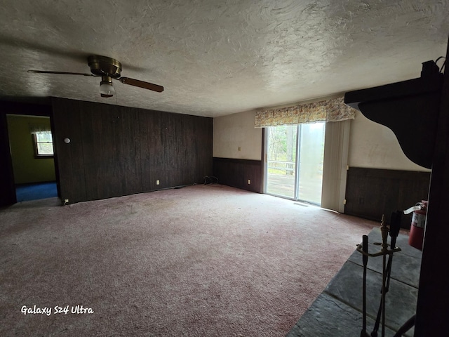 4591 Juneberry Trl, Gaylord, MI 49735 - unfurnished living room featuring wooden walls, healthy amount of natural light, carpet floors, a ceiling fan, and a textured ceiling