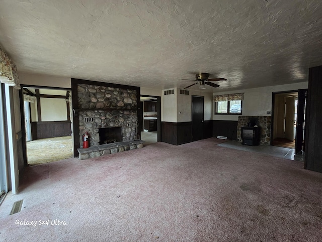 4591 Juneberry Trl, Gaylord, MI 49735 - unfurnished living room featuring carpet flooring, a ceiling fan, a stone fireplace, a textured ceiling, and a wood stove
