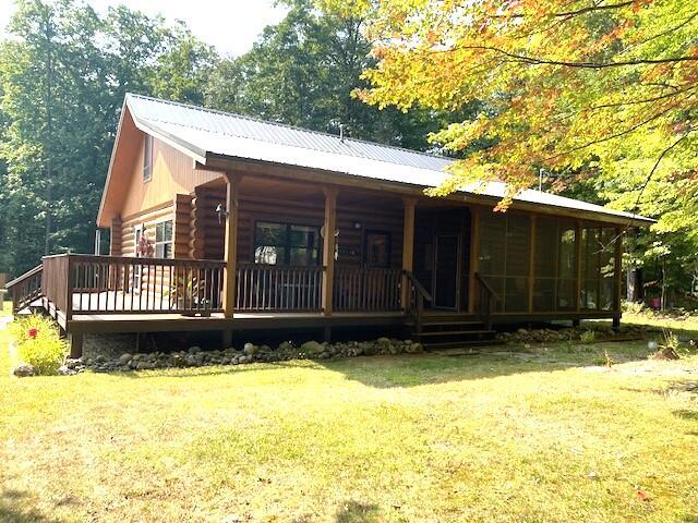 rear view of property featuring log siding, a lawn, covered porch, and metal roof