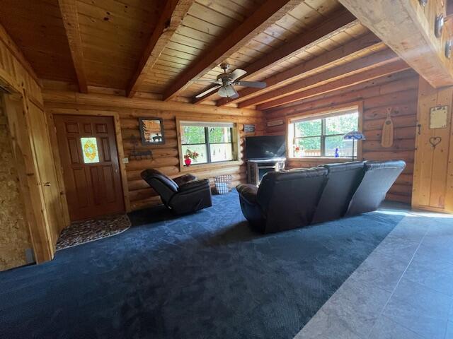 unfurnished living room featuring rustic walls, beamed ceiling, wood ceiling, and ceiling fan