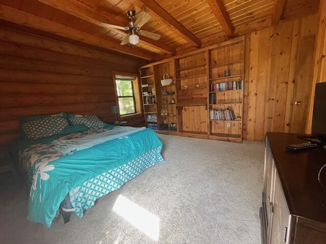 carpeted bedroom with beamed ceiling, wooden ceiling, and wooden walls