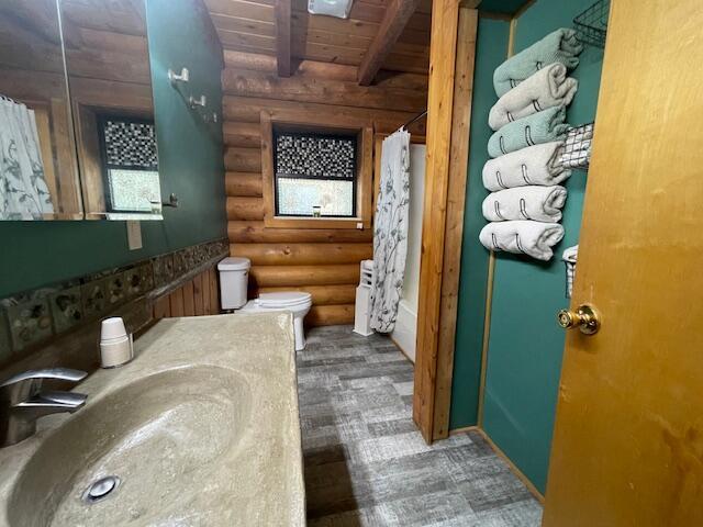 bathroom featuring toilet, wood ceiling, beam ceiling, wood finished floors, and log walls