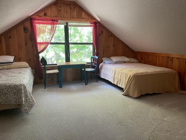 bedroom featuring light carpet, wooden walls, vaulted ceiling, and a textured ceiling