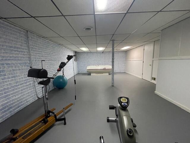 workout area featuring visible vents, a paneled ceiling, and brick wall