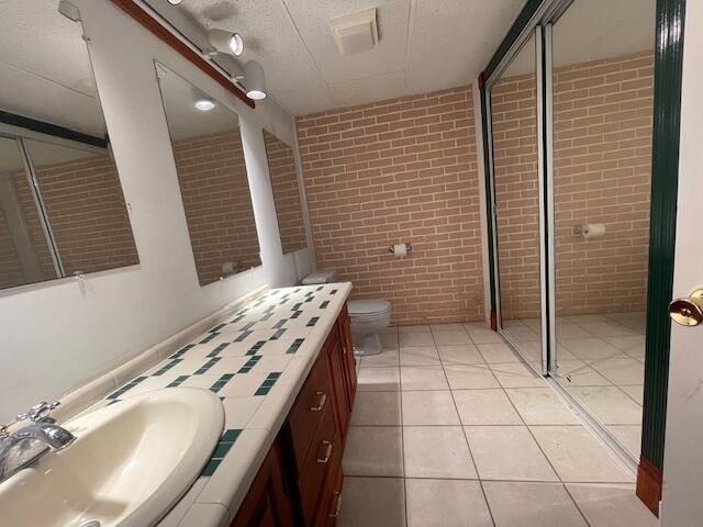 bathroom featuring vanity, brick wall, a textured ceiling, tile patterned floors, and toilet