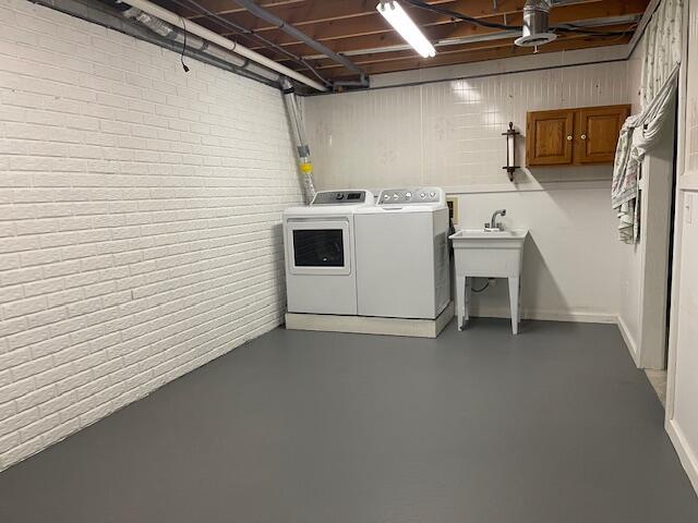 laundry room with laundry area, independent washer and dryer, brick wall, and a sink