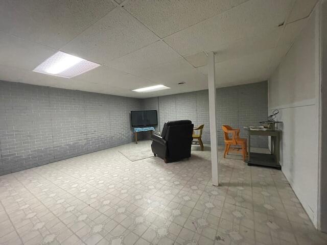 finished below grade area featuring tile patterned floors, a drop ceiling, and brick wall