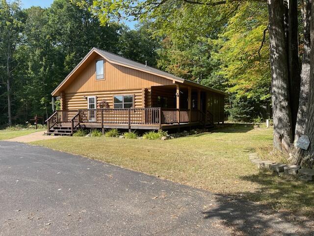 view of front of property featuring log exterior, a forest view, and a front lawn