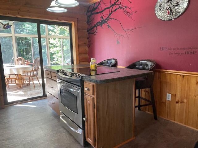 kitchen featuring dark countertops, wood walls, wainscoting, stainless steel range with electric stovetop, and log walls