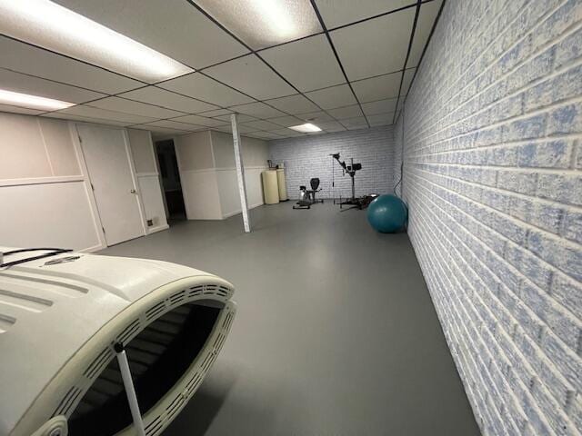 exercise room with brick wall and a drop ceiling