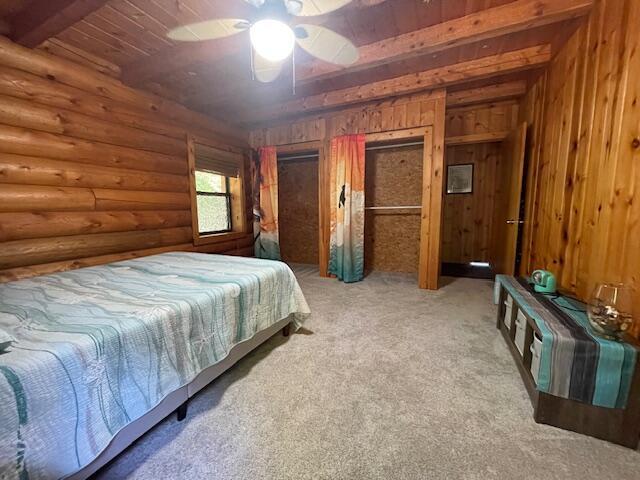 carpeted bedroom with ceiling fan, multiple closets, wood ceiling, beam ceiling, and log walls