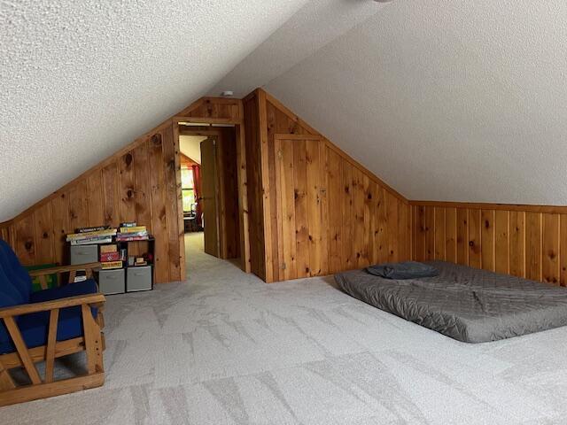 bedroom with lofted ceiling, wooden walls, carpet floors, and a textured ceiling