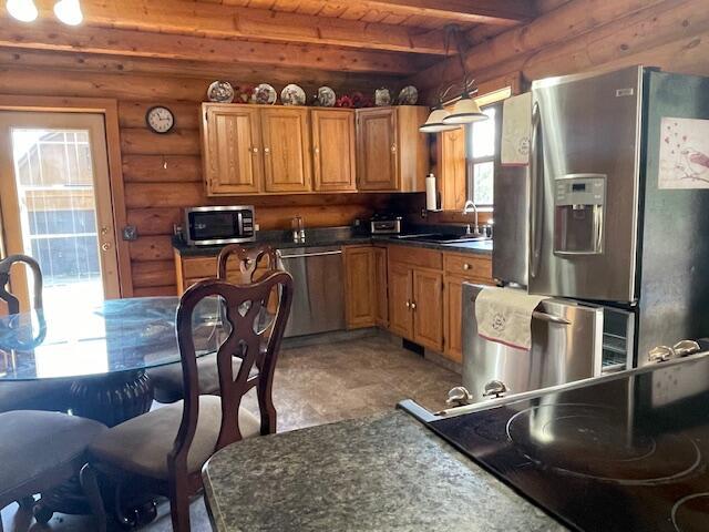 kitchen featuring dark countertops, beamed ceiling, appliances with stainless steel finishes, wooden ceiling, and rustic walls