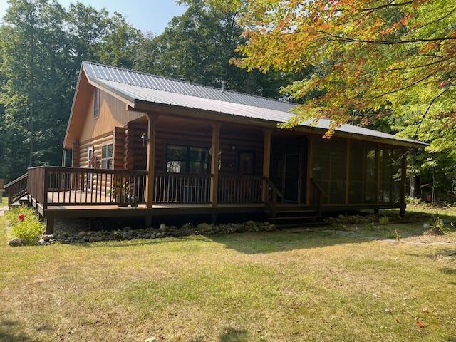 rear view of property with log exterior, a lawn, covered porch, and metal roof