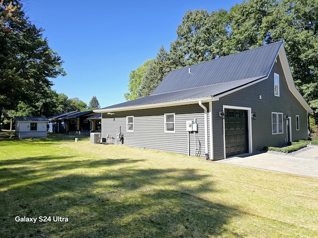 exterior space featuring central AC unit, driveway, a garage, a lawn, and metal roof