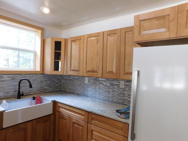 kitchen with backsplash, glass insert cabinets, light stone counters, freestanding refrigerator, and a sink