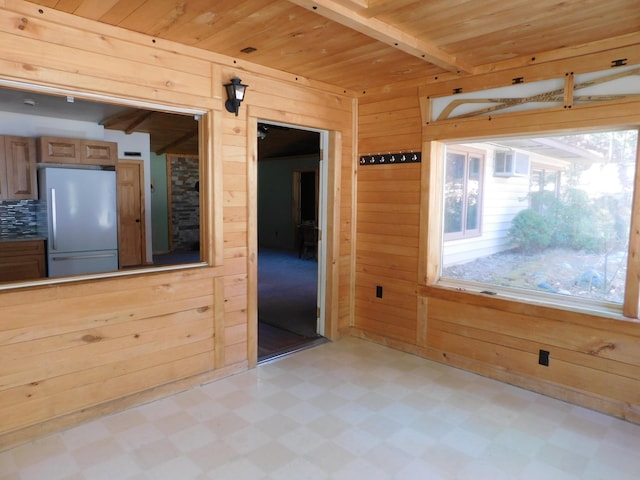 interior space with wooden walls, beamed ceiling, light floors, wooden ceiling, and refrigerator