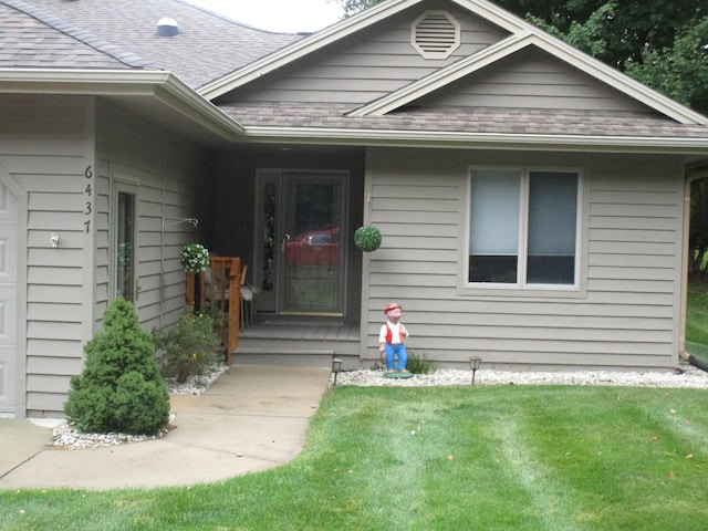 view of exterior entry featuring a garage, a yard, and a shingled roof