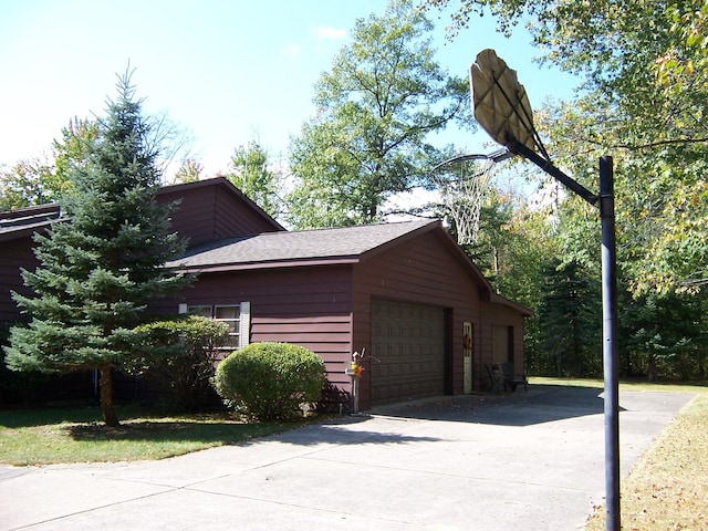 view of side of home featuring an attached garage, roof with shingles, and driveway