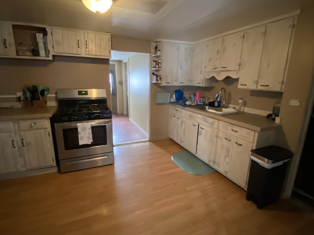 kitchen featuring stainless steel gas range oven, open shelves, light wood-style floors, white cabinetry, and a sink