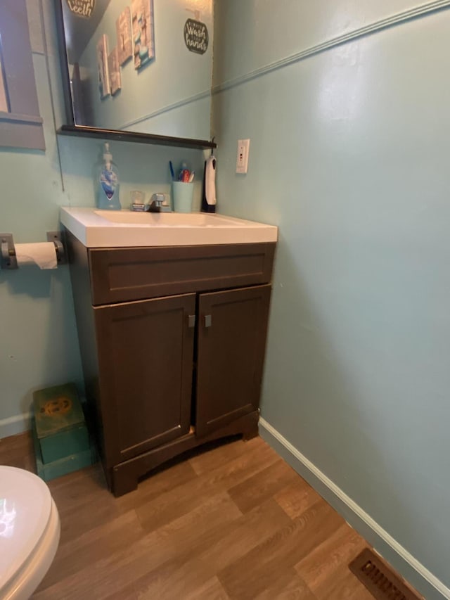 half bath featuring vanity, visible vents, wood finished floors, and baseboards