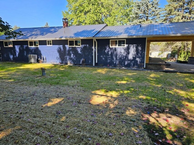 rear view of house with metal roof, a lawn, central AC, and a chimney