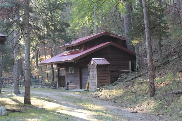 view of front of property featuring a view of trees, metal roof, a garage, and dirt driveway