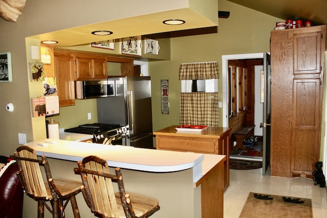 kitchen featuring light countertops, brown cabinets, a peninsula, a kitchen breakfast bar, and stainless steel appliances