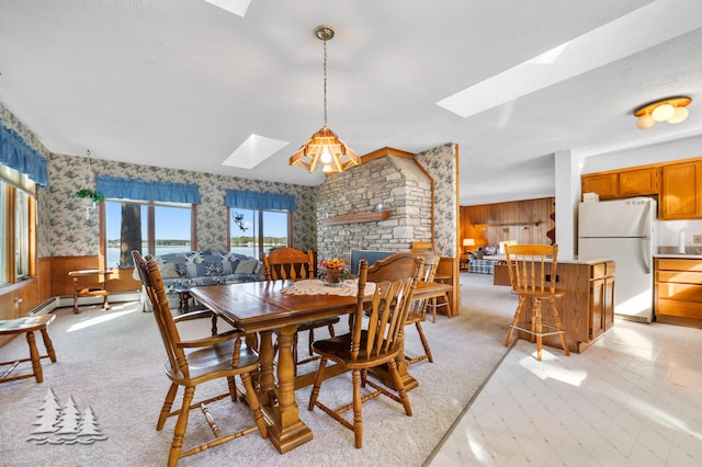 dining room with light floors, a wainscoted wall, wallpapered walls, a skylight, and a fireplace