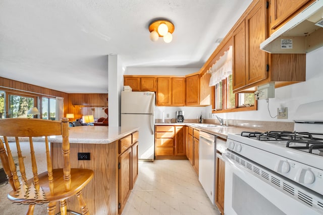 kitchen with under cabinet range hood, a sink, white appliances, light countertops, and light floors