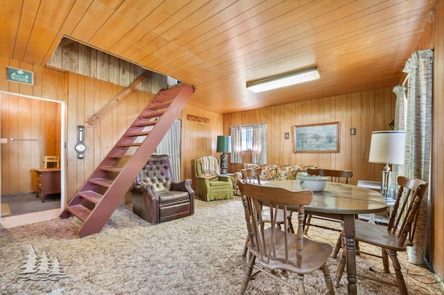 dining room featuring stairway, carpet flooring, wood ceiling, and wooden walls