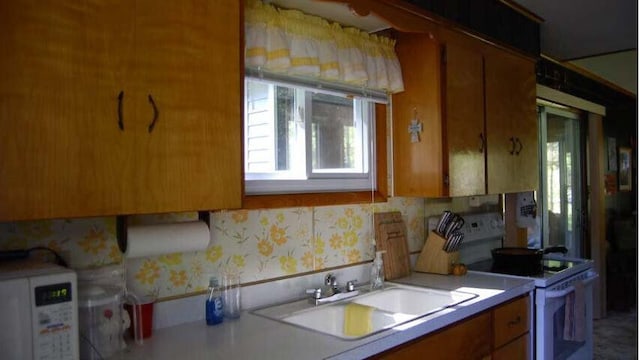 kitchen featuring a sink, wallpapered walls, white electric range oven, brown cabinetry, and light countertops