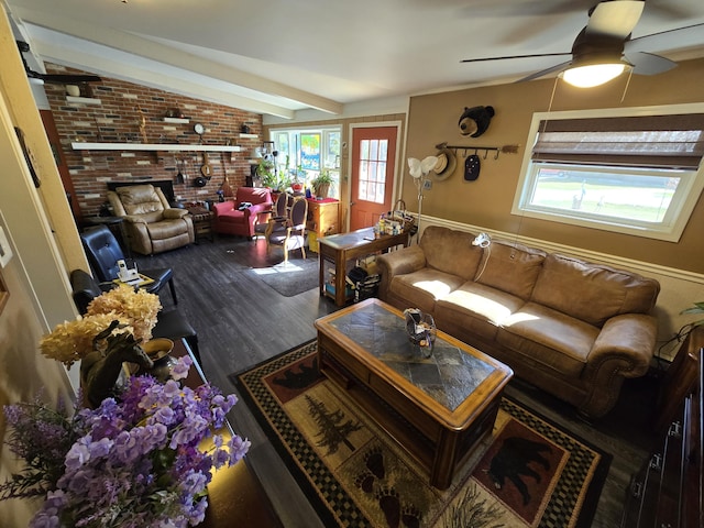 living area with brick wall, vaulted ceiling with beams, a fireplace, wood finished floors, and a ceiling fan