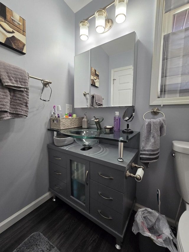 half bathroom with toilet, vanity, baseboards, and wood finished floors