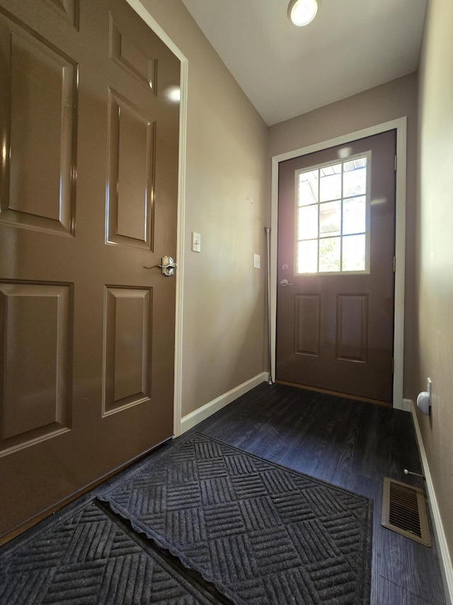 doorway to outside featuring dark wood finished floors, vaulted ceiling, baseboards, and visible vents