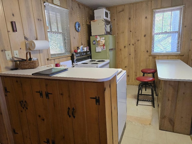 kitchen with white appliances, a peninsula, light countertops, wood walls, and brown cabinets