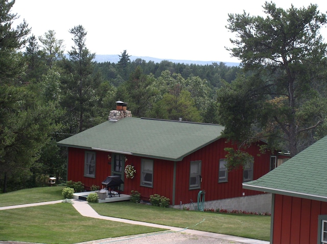 view of front of property featuring board and batten siding, a front lawn, and a forest view