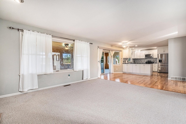 unfurnished living room featuring visible vents, baseboards, light colored carpet, and ceiling fan