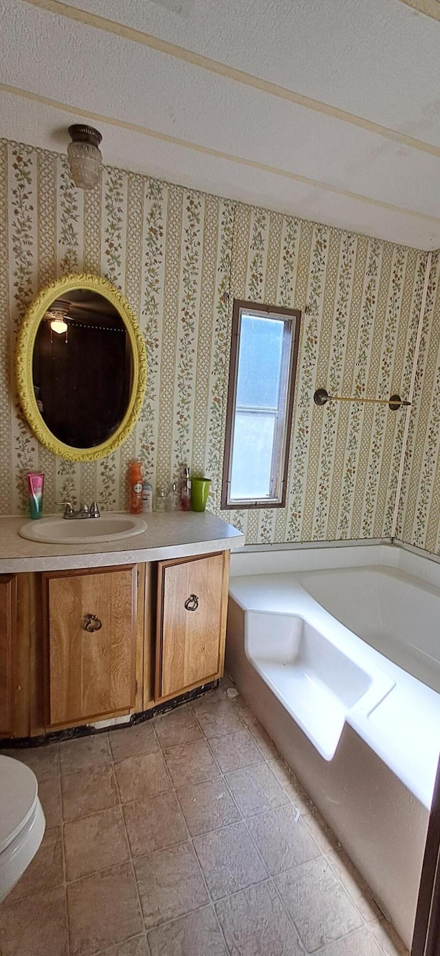 bathroom with a tub, wallpapered walls, toilet, vanity, and a textured ceiling