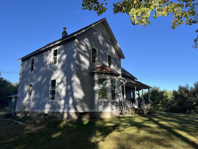 view of side of property featuring a lawn, covered porch, and a chimney