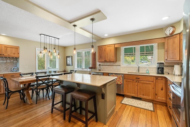 kitchen featuring a sink, a kitchen island, backsplash, stainless steel appliances, and light wood-style floors