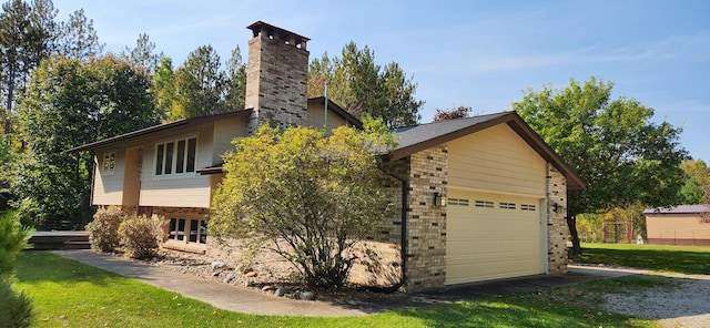 exterior space with a garage, a lawn, a chimney, and brick siding