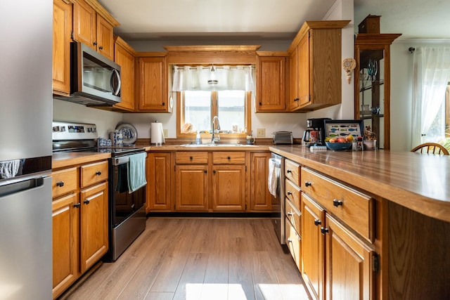 kitchen with brown cabinetry, light wood finished floors, a sink, butcher block countertops, and stainless steel appliances